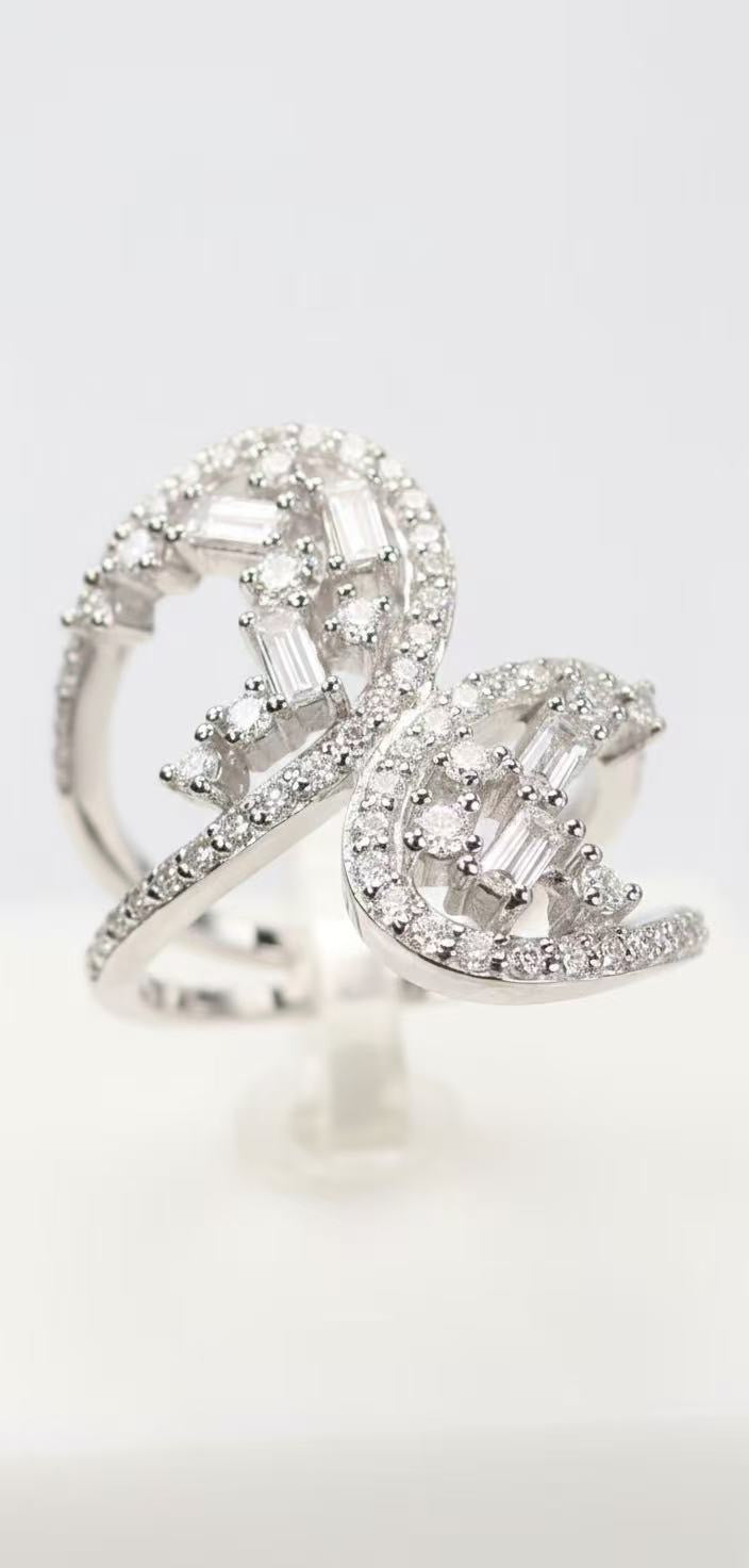 sterling silver bypass statement ring featuring two mirrored scroll-shaped arms, each set with scattered-angle baguette-cut and round brilliant-cut stones in pavé and prong settings, open center design with visible negative space, shown on white background (image 1) and worn on ring finger (image 2)
